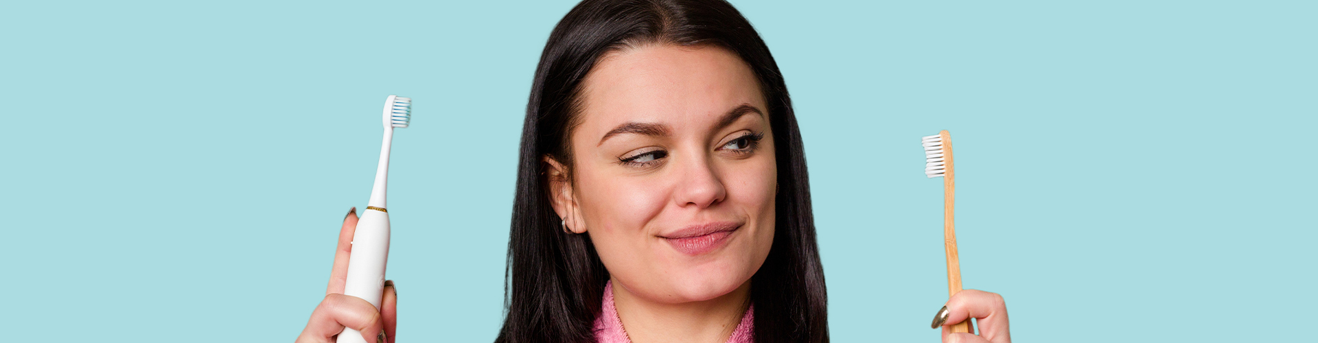 Woman in pink robe holding electric and manual toothbrushes.